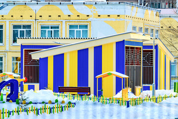 New colorful modern kindergarten building with playgrounds in snowy winter.