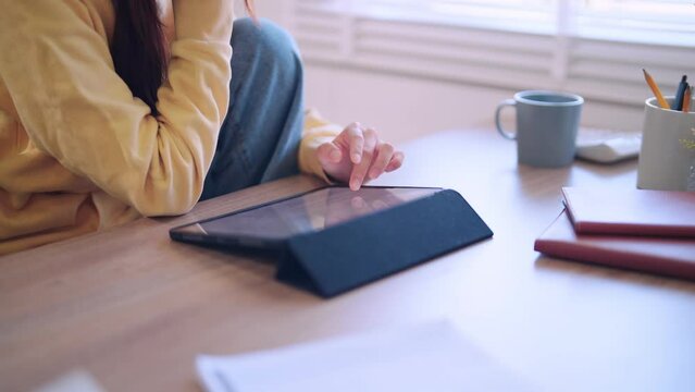Asian female student attentively reads lesson content or articles online through her tablet at the home desk