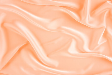 Peach silk background. Wavy folds peach silk texture satin material. Color of the Year 2024. Peach fuzz