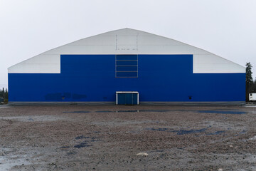 Fototapeta na wymiar Blue and white sports arena building with gravel parking