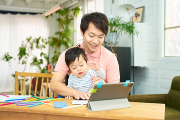 赤ちゃんを抱えて自宅でパソコンを操作する男性