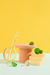 Fresh pennywort leaves adorn wooden platforms amid glassware on a yellow-white backdrop, creating a sophisticated setting to showcase cosmetics enriched with Centella extract.