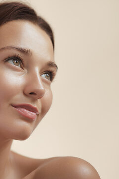 Skincare Beauty Spa Face of Woman with Healthy Skin, Natural Makeup .Young adult happy girl model with bare shoulders on beige background closeup. High-quality beauty product or treatment conceptual