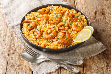 Shrimp risotto is made with fragrant arborio rice sauteed in onions and garlic, simmered stock, and topped with seasoned shrimp closeup on the plate on the wooden table. Horizontal