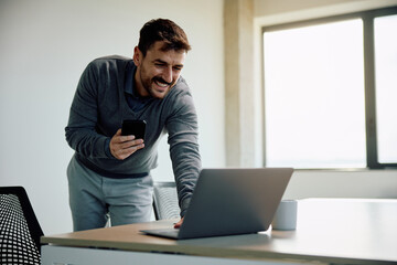 Happy businessman using laptop while working in office.