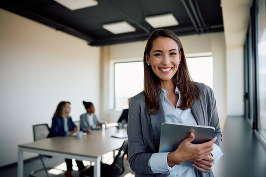Young happy businesswoman using digital tablet in meeting room and looking at camera.