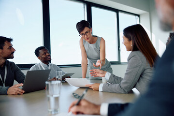 Female CEO talks to group of her colleagues in meeting room.