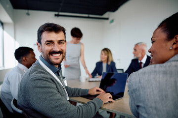 Happy businessman using laptop during meeting and looking at camera.