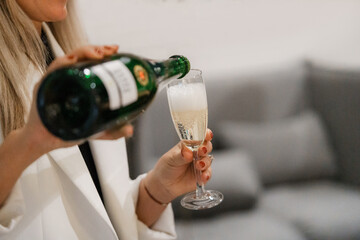 Close-up of female hands pouring champagne into glass. Blurred background.