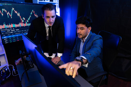 Two stock traders discussing dynamic currency market graph on real time monitor. One of investor pointing on highest profit point on database network economic online technology investment. Sellable.