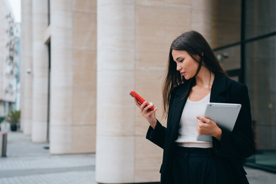 successful girl, lawyer stands outside courthouse, reads messages on phone, holds tablet and studies new information. Asian businesswoman waiting for  client to go to business meeting in office