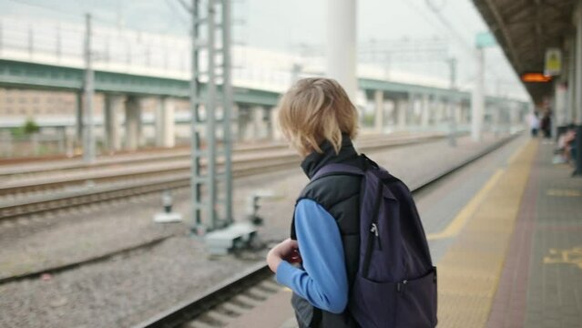 A cute teenage boy is waiting for a train on a railway platform or subway station. Metropolis transport system. Public transport in a big city