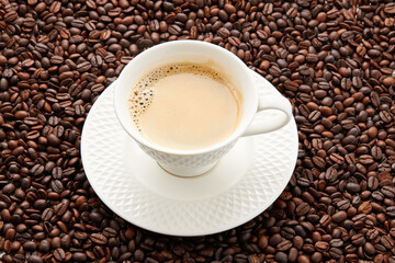 Top view of coffee in white cup place on surface many roasted coffee beans background.