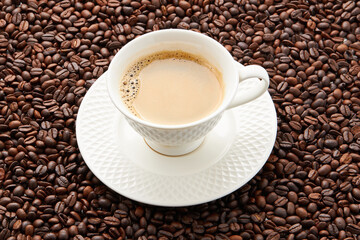 Top view of coffee in white cup place on surface many roasted coffee beans background.
