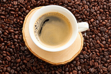 Top view of coffee in white cup place on surface many roasted coffee beans background.
