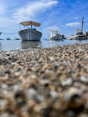 Fototapeta na wymiar Small boat anchored on calm sea by the pebble beach. Selective focus. 