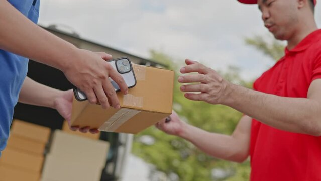 Delivery man, driver in red orange uniform is sending parcel box package from cargo truck at home to customer' hands then sign and cash on delivery for parcel by cross-border QR payment