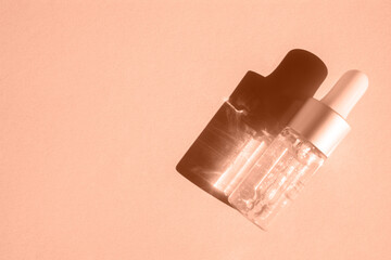 A glass dropper bottle with cosmetic lotion on a solid background casts a shadow. Top view, place...