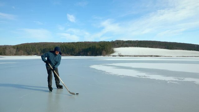 An elderly man practices stricking the puck with hockey sticks on a frozen lake in winter.