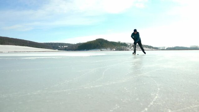 An elderly man practices stricking the puck with hockey sticks on a frozen lake in winter.