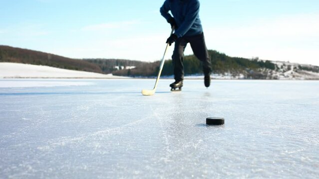 An elderly man practices stricking the puck with hockey stick on a frozen lake in winter.