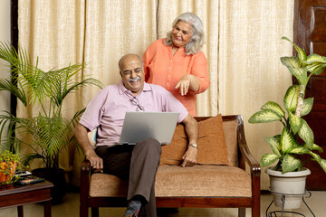Obraz premium Indian senior couple Having fun together at home sitting at sofa in living room