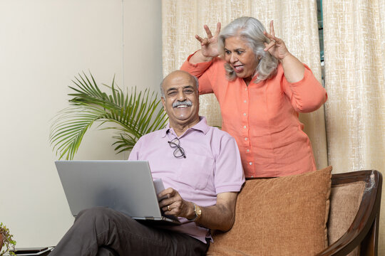 Indian senior woman teasing husband in living room , After retirement life enjoyment