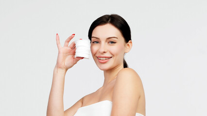 Charismatic, beautiful young woman using a cotton pad on a light isolated background. Concept of clean skin, facial care and natural cosmetics.