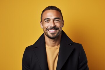 Portrait of smiling man in black coat and yellow sweater on yellow background