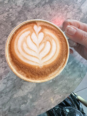 female hand holds cup of latte coffee with heart