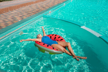 Happy woman in a swimsuit and sunglasses floating on an inflatable ring in the form of a watermelon, in the pool during summer holidays and vacations. Summer concept.