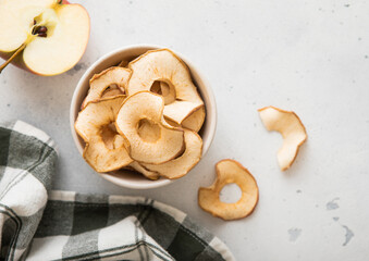 Top view of bowl with dried apple rings on light background with ripe apple slice and kitchen towel.Macro.