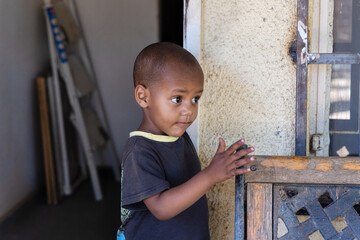 mixed race boy playing on an forged iron bench in front of the house - obrazy, fototapety, plakaty