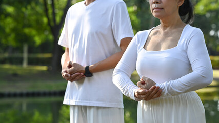 Calm senior people in white clothes doing breathing exercise while standing amidst nature