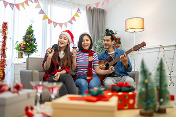 Happy friends celebrating Christmas together.Asian man playing guitar in living room full decoration with Xmas tree.