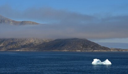  an iceberg, low lying clouds, and hillside,  near nanortalik near tasermiut fjord  in southern...