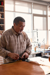 serious thoughtful man going to brushcloth, craftsman holding brush , standing behind table tailor...