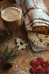 Christmas stollen with coffee cup and decoration toys. Sweet Christmas bread with cacao and powdered sugar. New Year decor. Homemade stollen with raisins on festive table. Winter breakfast. 