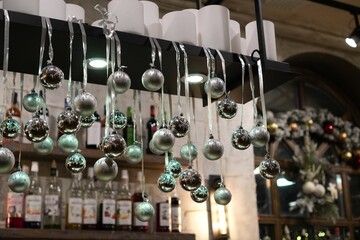 festive winter interior decoration with silver balls on ribbons on the background of shelves with bottles and an arched mirror with a wooden frame in a cafe in December in winter