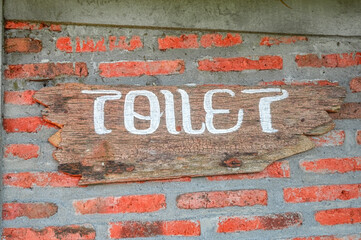 a wooden sign that says toilet is attached to a brick wall