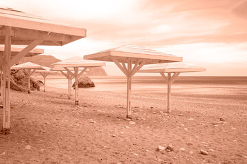 Wooden awnings on a deserted sandy beach overlooking the sea. Trendy color of year 2024 - Peach Fuzz.