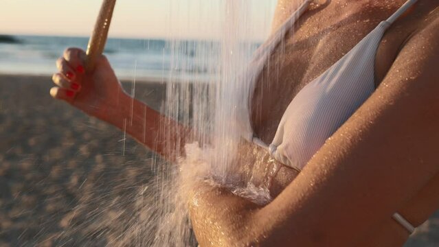 A beautiful young woman in a white swimsuit takes a shower on the beach by the sea. drops close-up. Attractive young woman enjoying a shower at sunset after swimming. Holidays at sea.
