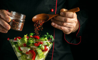 The chef is preparing a fresh vegetable salad for lunch. Adding aromatic spices to a bowl of...