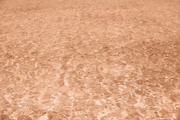 sun glare in water in pastel peach color background and texture. Peach fuzz color of the year.