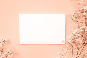A blank sheet of paper on a background color and natural delicate flowers. Flat lay, place for text. Trendy color of year 2024 - Peach Fuzz.