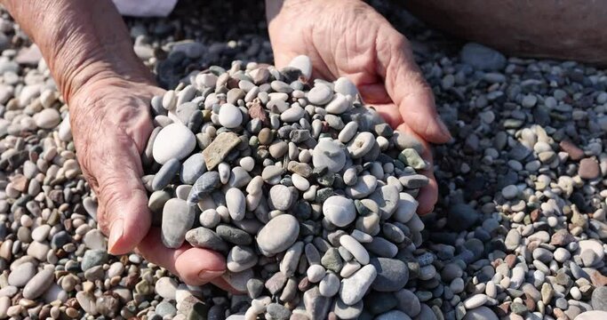 Hands of elderly woman holds handful of stones on beach. Gifts of nature and power of water protect stones
