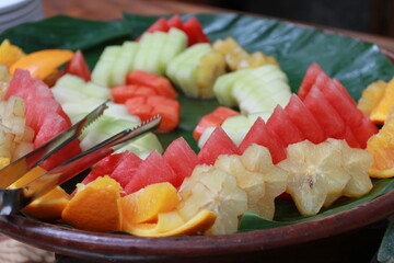 Assorted fresh fruit slices for deserts on wooden plate with banana leaf.