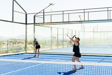 Fototapeta na wymiar Active women doing a padel tennis serve exercising