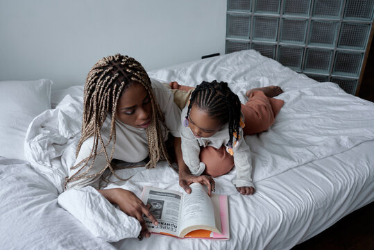 young woman with dreads showing magazine to her child, close up photo. woman teaching her kid to read
