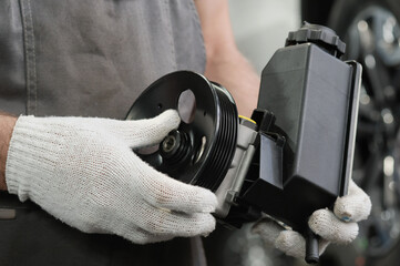 A power steering pump is in the hands of an auto mechanic. Inspection of a new product before replacing a defective part.